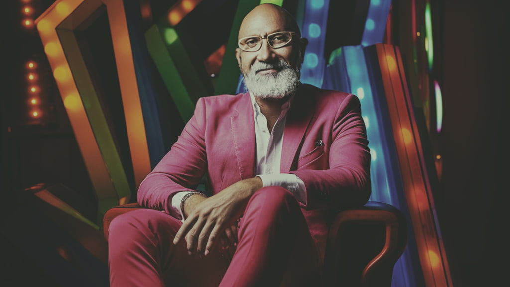 A male figure in a pink suit between colourful vertical bands.